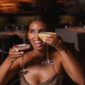 lady holding two drinks in her hands and enjoyung the vibes at three cuts steakhouse and bar during happy hour